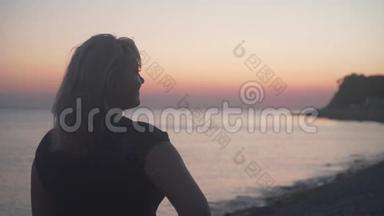 一个女人站在海上日落的背景上。 一个女人背对着镜头站在海滩上。